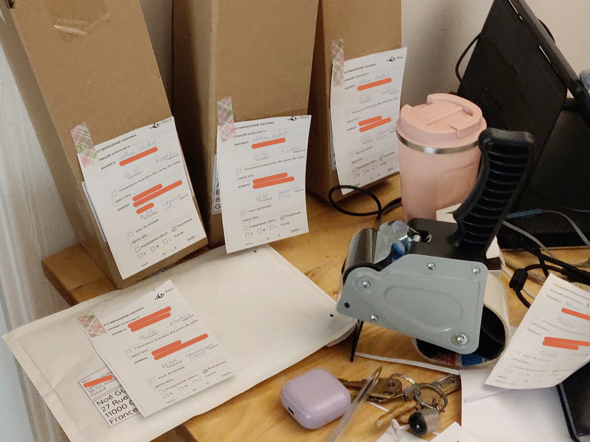 3 cardboard box are sitting on a desk with a enveloppe, a pink coffee cup, a tape dispenser, earbuds and keys. It's a big mess.